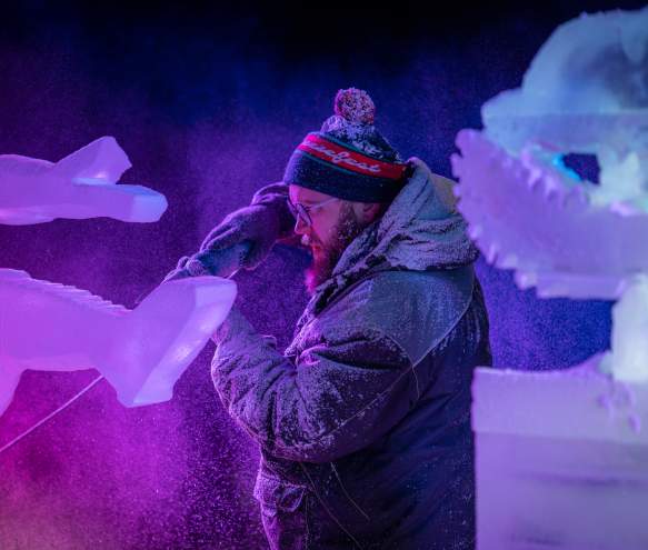 An ice sculptor using a power tool to carve a block of ice at the Freezefest ice battle