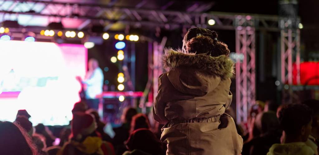 Girl sitting on man's shoulders to see guitarist on stage at Countdown to Christmas event