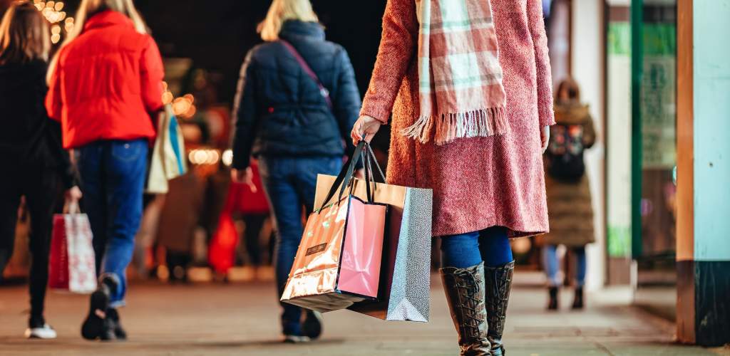 Lady dressed in light pink jacket and scarf carrying a bundle of Christmas shopping