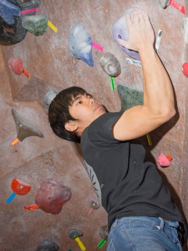 An Asian boy grips to rubber rocks while climbing an indoor rock climbing wall