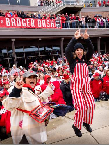 Three women dressed in UW badger gear jumping and cheering with a crowd of Badger fans behind them.