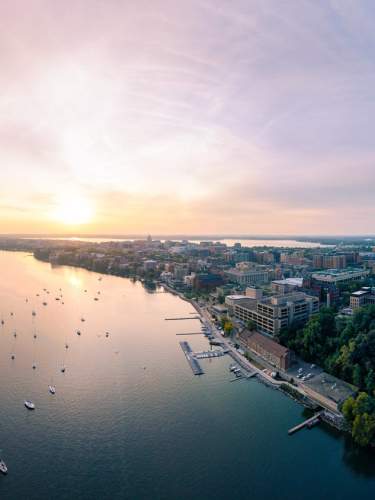 A wide drone image of the city at sunset with Lake Mendota in the foreground