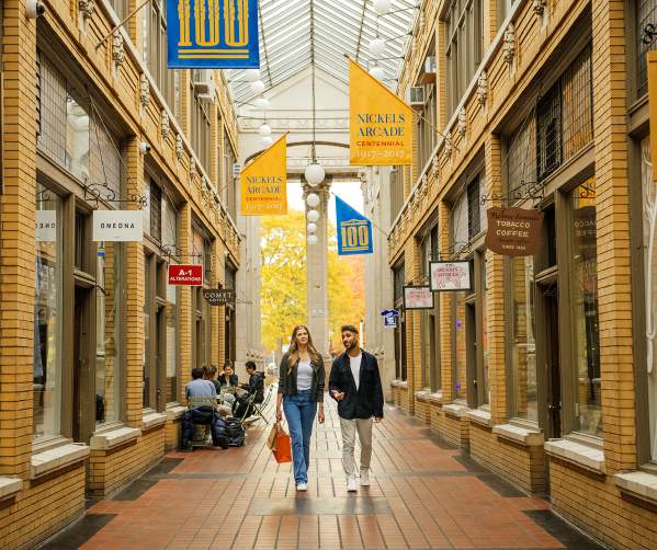 Couple walking in the center of a brick corridor with a glass roof, at Nickels Arcade