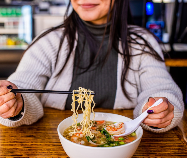 woman smiling while using chopsticks to eat a bowl of ramen