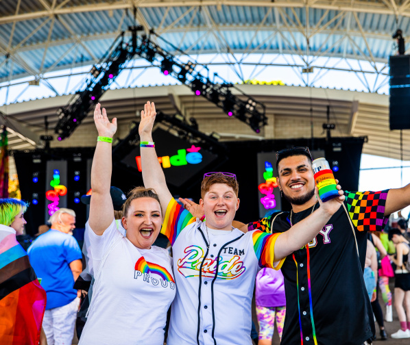 three friends cheering in front of a stage at pridefest