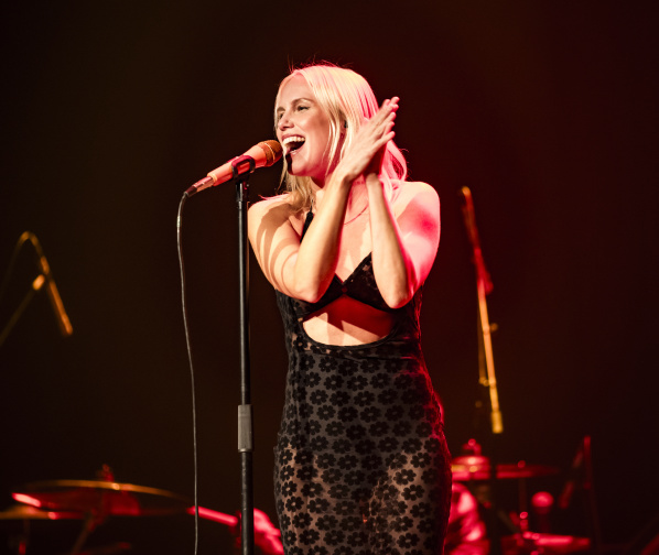 Grace Weber smiling as she sings into a standing microphone and claps