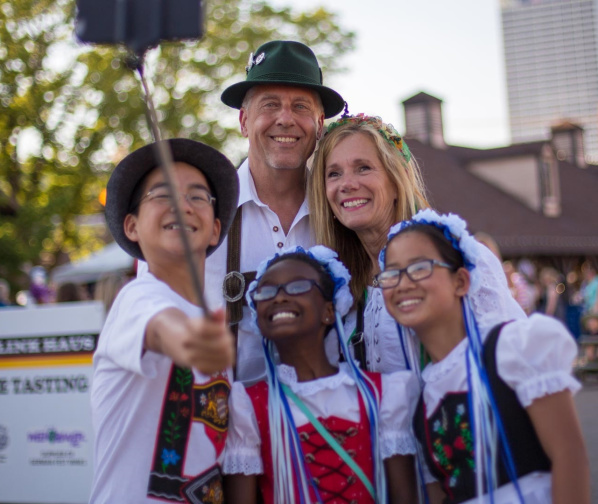 a family taking a selfie with a selfie stick in traditional German attire on festival grounds