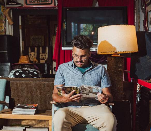 A person sits reading a magazine in a laid-back shop space with skateboards, posters, and eclectic vintage items.