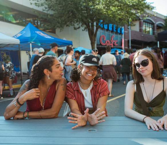 Three friends sitting at a picnic table teasing an goofing around with each other.