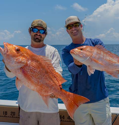 Two men on a boat each holding up their Red Snapper fish catch