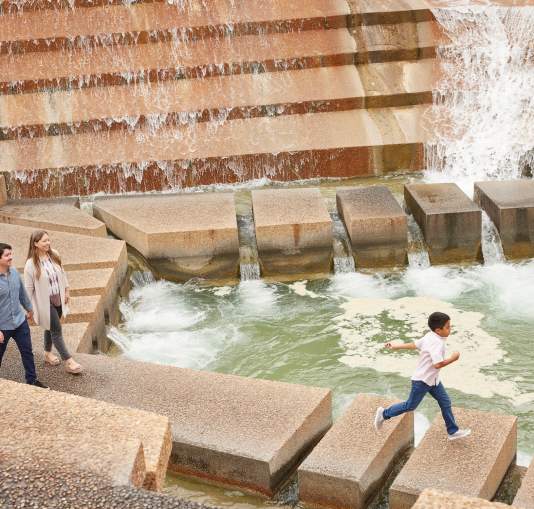 Visitors walking along concrete steps beside cascading water features and pools at the Fort Worth Water Gardens in downtown Fort Worth.