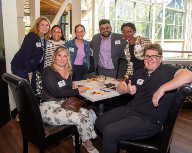 A group photo of people sitting and standing around a table posing for the picture.