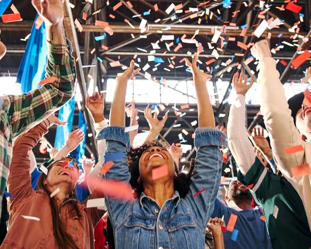 People with their arms up, cheering and confetti falls on them