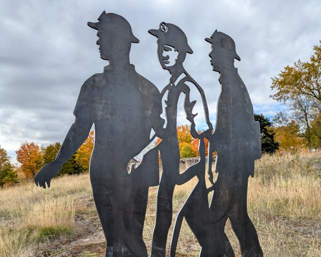 a trio of steel-cut miner silhouettes agains fall trees