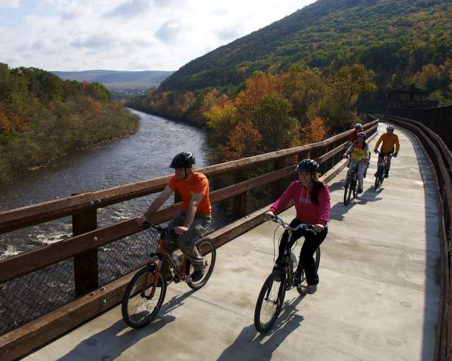 Family bikes across a bridge with mountains and river in the background