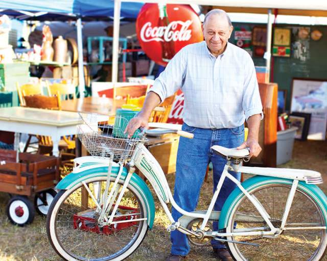 Man posing for a picture with an old bike during the Liberty Antiques Festival now in Ramseur, NC