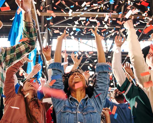 People with their arms up, cheering and confetti falls on them