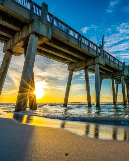 sunlight peering behind a dock by the ocean waters of pensacola beach