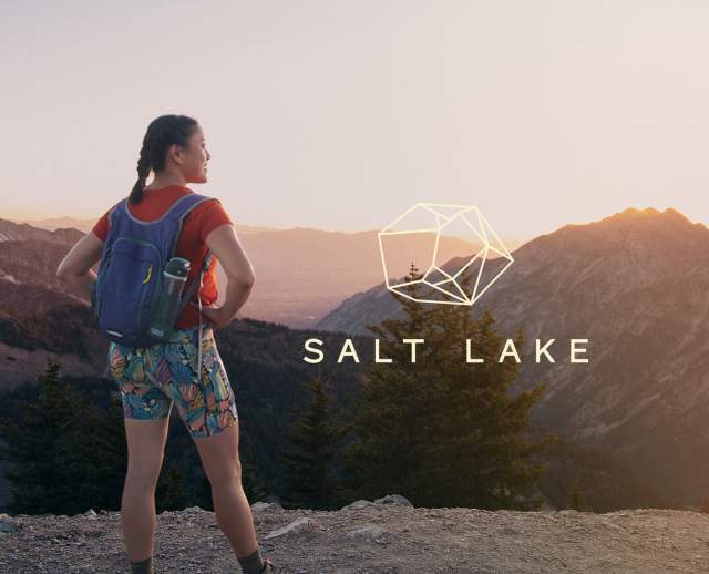 Person standing with backpack on in front of sunrise over mountain tops. On the right side of the image a vertical mountain range has West of Conventional on it