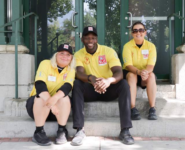 Three people sitting on steps wearing yellow downtown ambassadors shirts