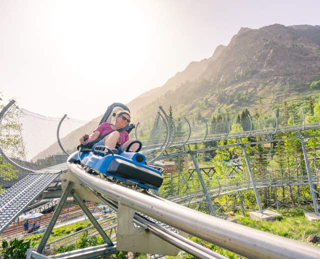 Woman looking like she is going fast around a corner on a single person coaster with sky and mountains around her