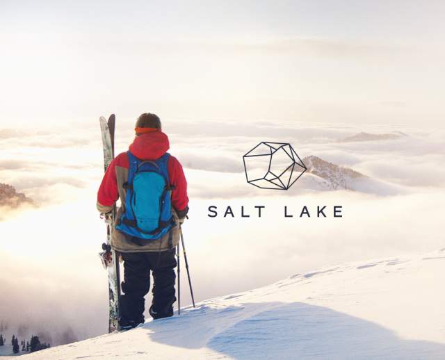 A skier holding skis looking out over a valley filled with clouds with Salt Lake and West of Conventional written on it.