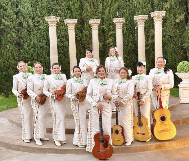 10 women posing with instruments in white traditional mariachi dress