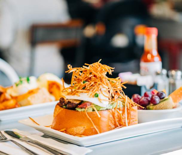A B&B Burger from Bacon and Butter with a side of fruit and more food in the background on a white tray.