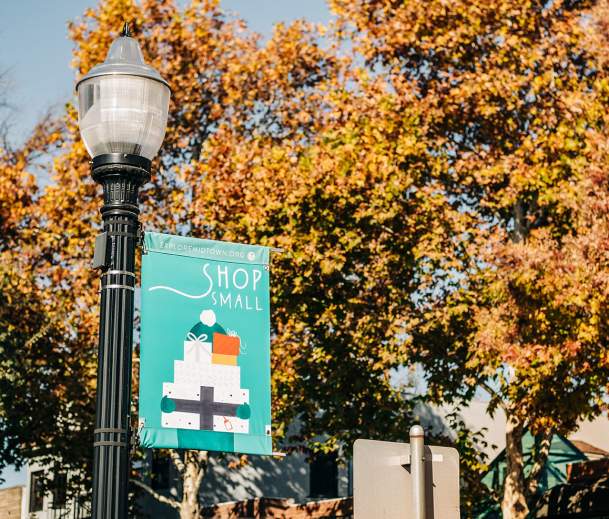 street banner that says shop small and has someone holding gifts