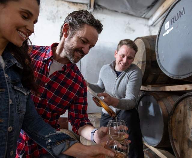Couple enjoying a tour at Killowen Distillery while the guide pours liquid into their glasses for sampling