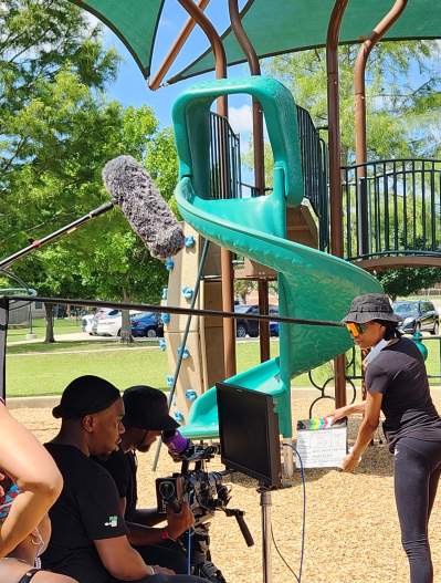 Film crew with cameras, mic, and clap board - adults and children at a playground