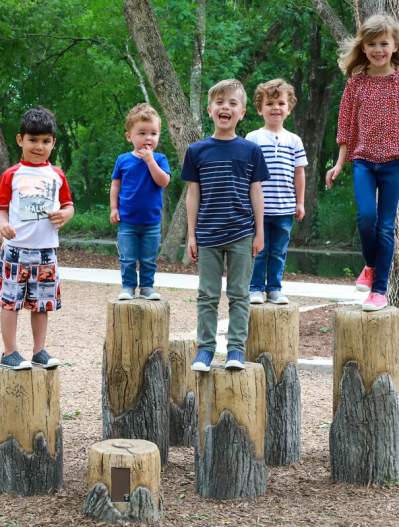 kids standing on tree stumps at varying heights in a park