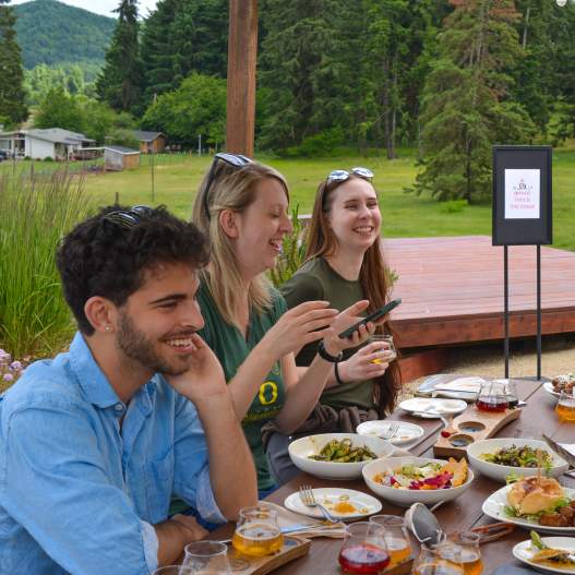 Five people enjoying food and beverage at a picnic table.