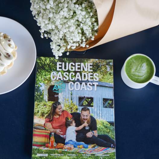 A visitor guide sits on a blue table with a matcha latte, a pastry and a small bouquet of flowers.