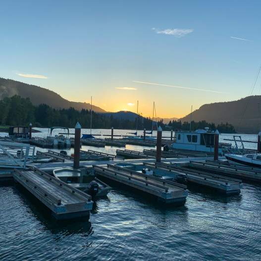 Docks on a lake with the sun rising over the mountains in the distance.