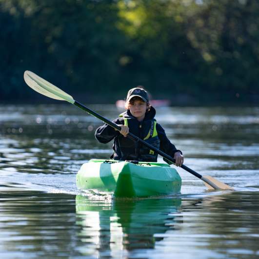 A person paddling on a river in a kayak.