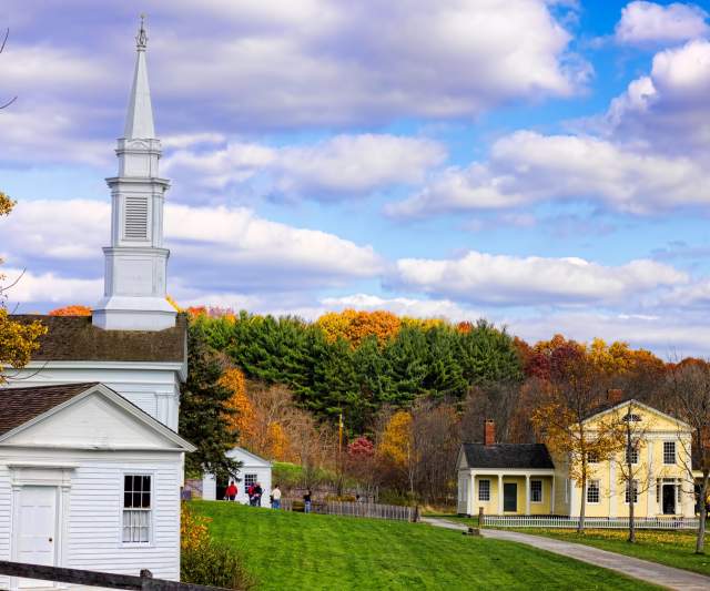 Akron scenic view of historic buildings with autumn foliage, showcasing a church and two houses under a partly cloudy sky.