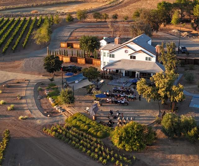 A white craftsman style tasting room amid vineyards and trees at sunset