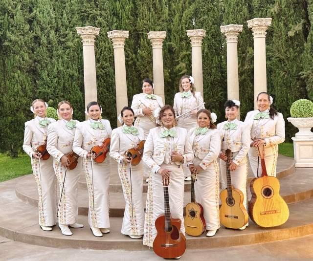 10 women posing with instruments in white traditional mariachi dress