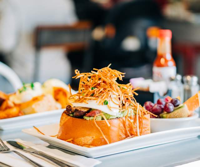 A B&B Burger from Bacon and Butter with a side of fruit and more food in the background on a white tray.