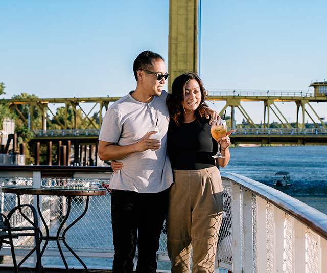 A smiling couple enjoying beverages and riverfront views