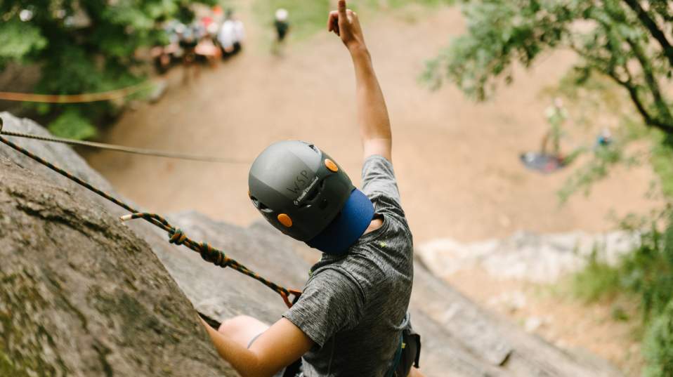 Man rock climbing on a cliff giving a thumbs up