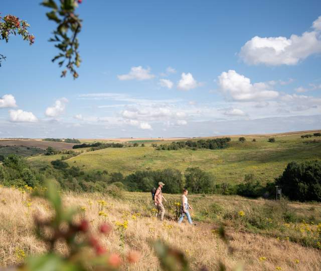 Two people walking along path on hillside with countryside in background and blue skies