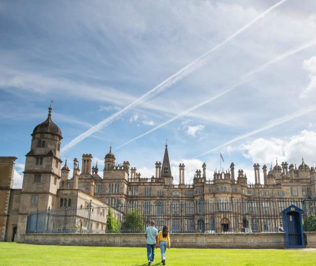Two people walking towards the gates of Burghley House in Stamford