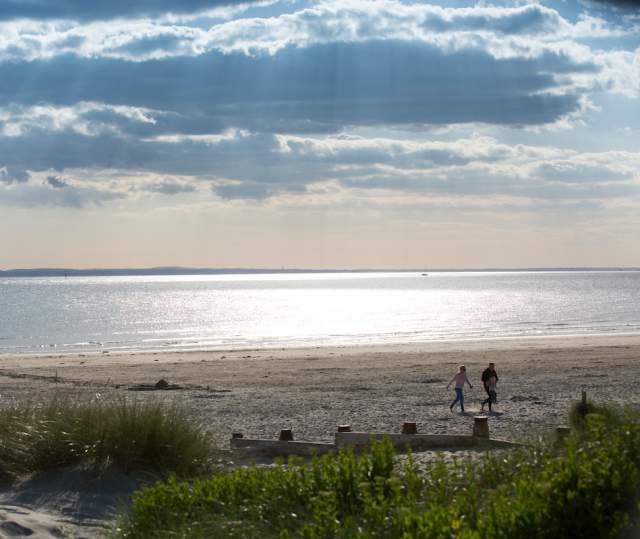 Sunny day at West Wittering beach looking out to sea, with a couple walking in the sandy dunes