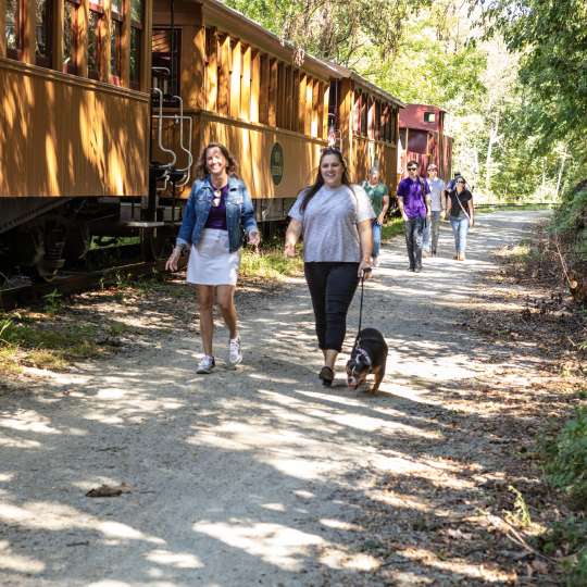 two people walking on rail trail with their dog next to northern central railway of york's steam engine