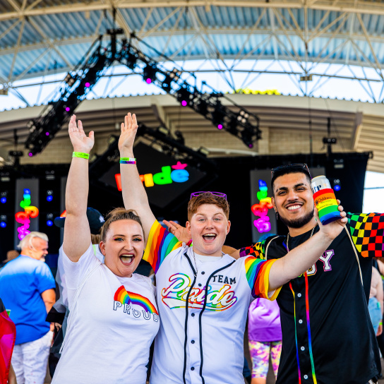 three friends cheering in front of a stage at pridefest