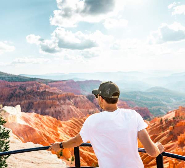 Person standing at scenic overlook at Cedar Breaks National Monument with a red rock canyon in the background and blue skies.