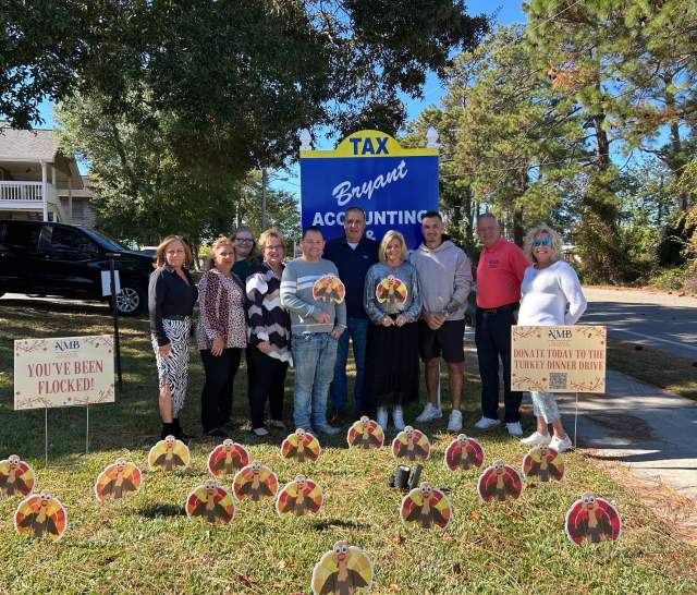 Group of people surrounded by a display of cardboard turkey cut-outs in front of a local business.
