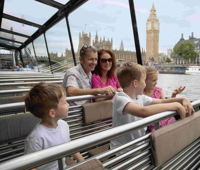 Family sat on top of cruise boat on the Thames with Houses of Parliament and Big Ben in the background